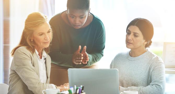 Photo of three adult women of different races having a serious discussion around a computer