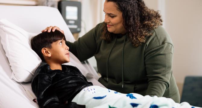 Photo of a boy in a hospital bed with a woman helping him with her hand on his forehead